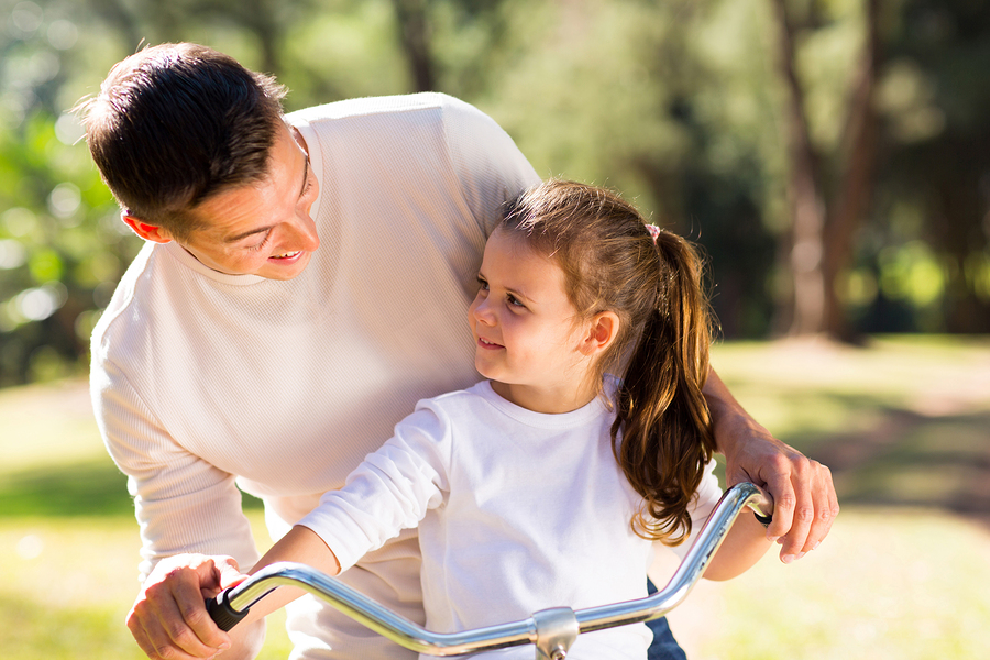 happy young father riding bicycle with his daughter outdoors